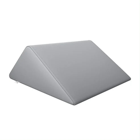 DIR Gray triangular foam bolster pillow providing leg and back support on a massage bed.