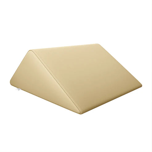 DIR Beige triangular foam bolster pillow providing leg and back support on a massage bed.